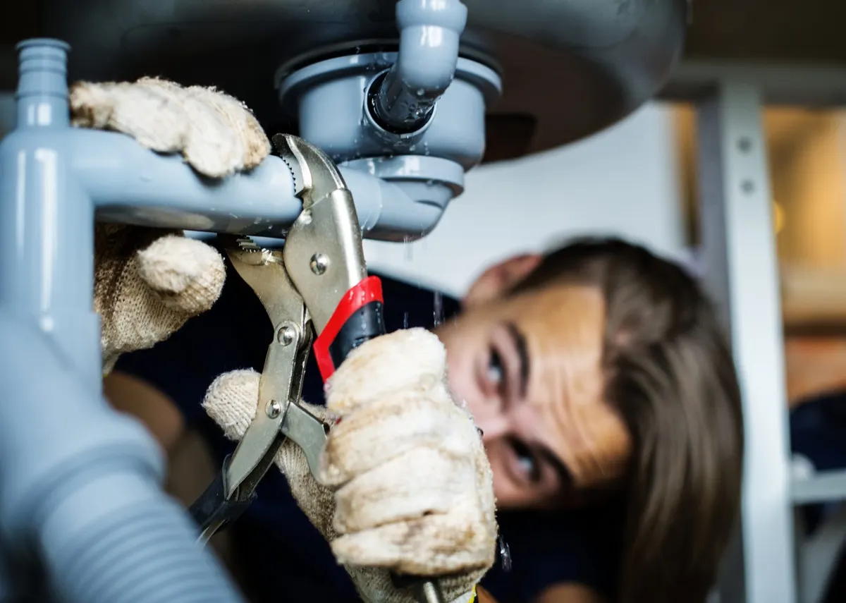 Plumber repairing a leaking pipe under a sink